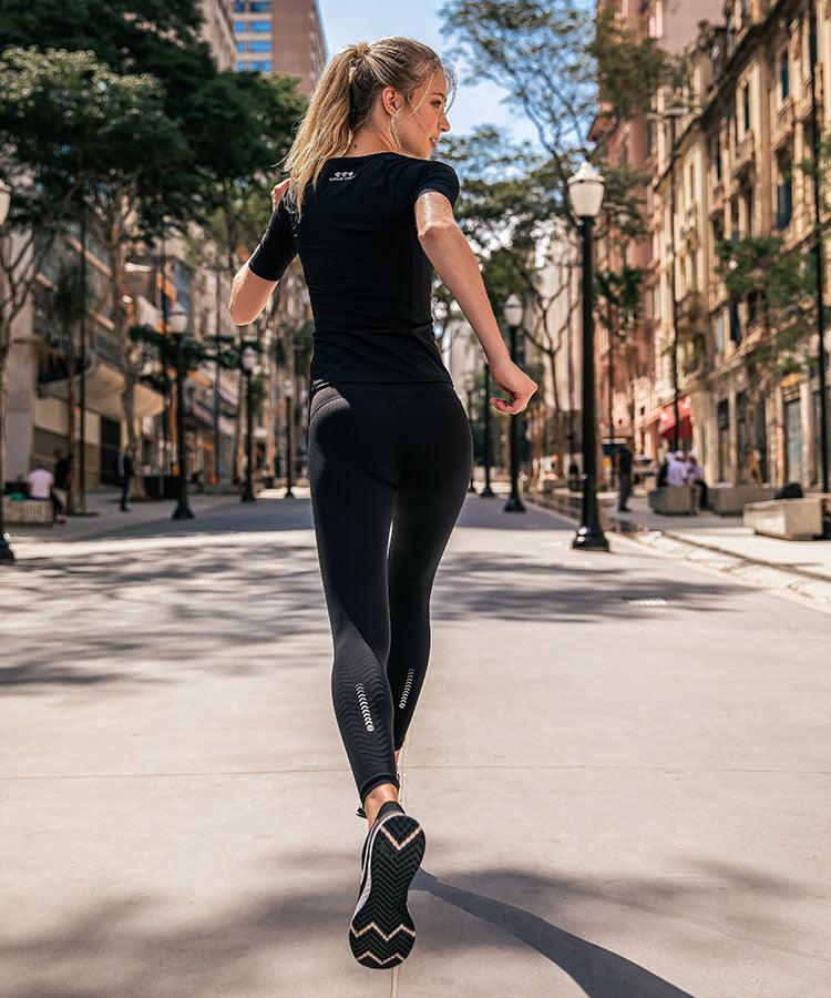 Woman running in city back view wearing WaveWear Y20 Classic Knee and Calf Recovery Tape Compression Leggings in black showing calf taping pattern with black top and sneakers