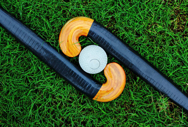 Close up of two field hockey sticks laying opposite of each other with a ball in the middle laying on turf