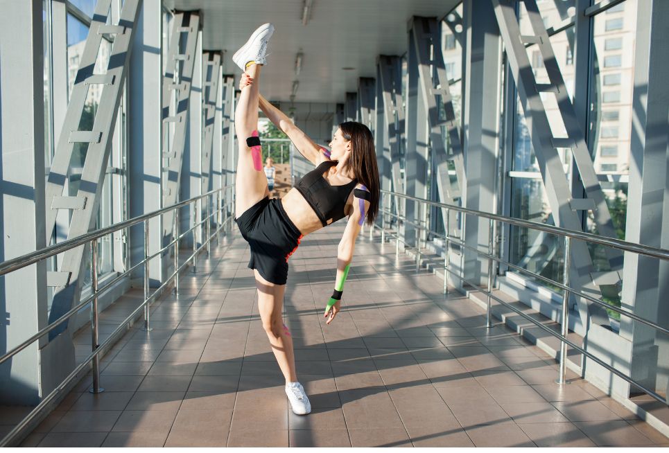 Athlete stretching leg with kinesiology tape applied on knee and arm demonstrating kinesiology tape pros and cons