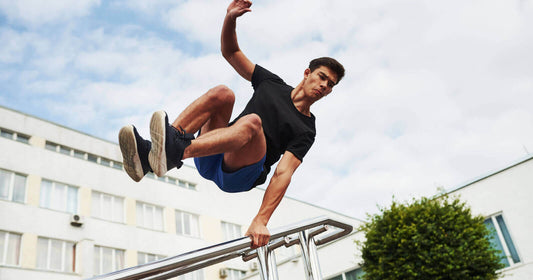 Young man practicing parkour basics for beginners by vaulting over a metal railing outdoors