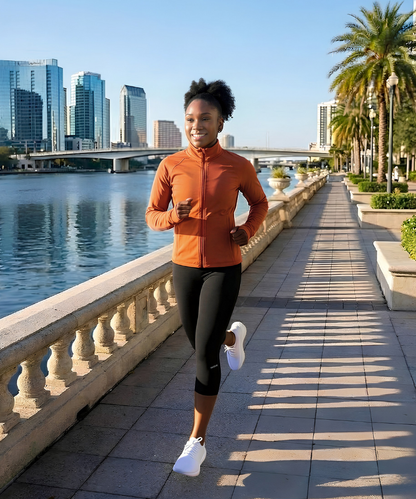 Woman running along waterfront promenade wearing CY20 3/4 Capri Compression Leggings with orange running jacket in city setting