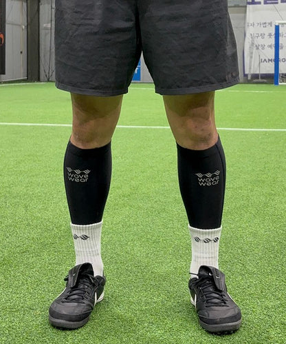 WaveWear C2 Calf Recovery Kinesiology Compression Sleeves in black worn by football player on synthetic turf back view