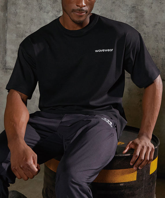 WaveWear black dynamic oversized fit t-shirt worn by a man sitting on a barrel in casual setting