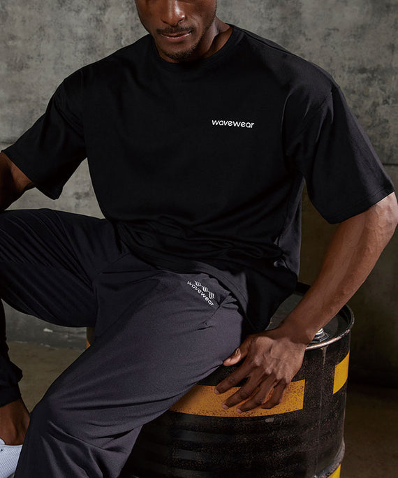 WaveWear black dynamic oversized fit t-shirt worn by man sitting on industrial barrel