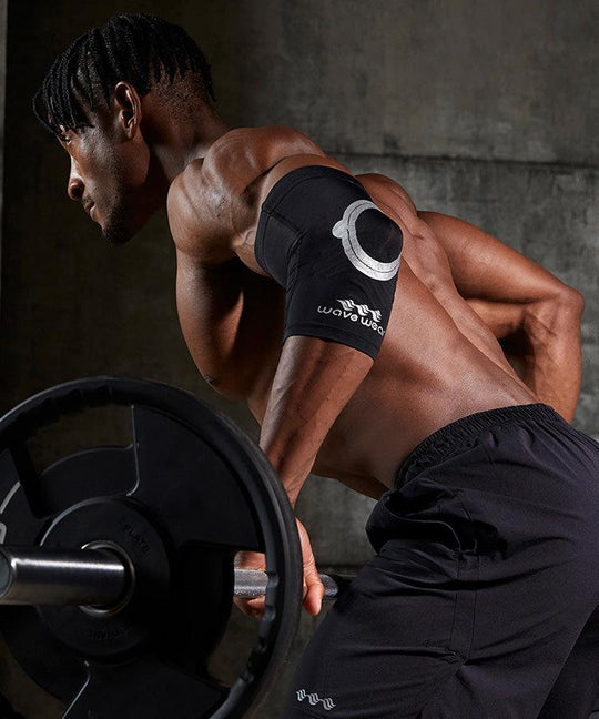 Black E2 elbow sleeve worn while gripping barbell during workout, gym setting