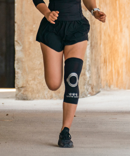 Schwarze K2 Kniebandage bei einem Läufer im Schritt, mit sichtbarem rundem Patella-Pad auf der Straße