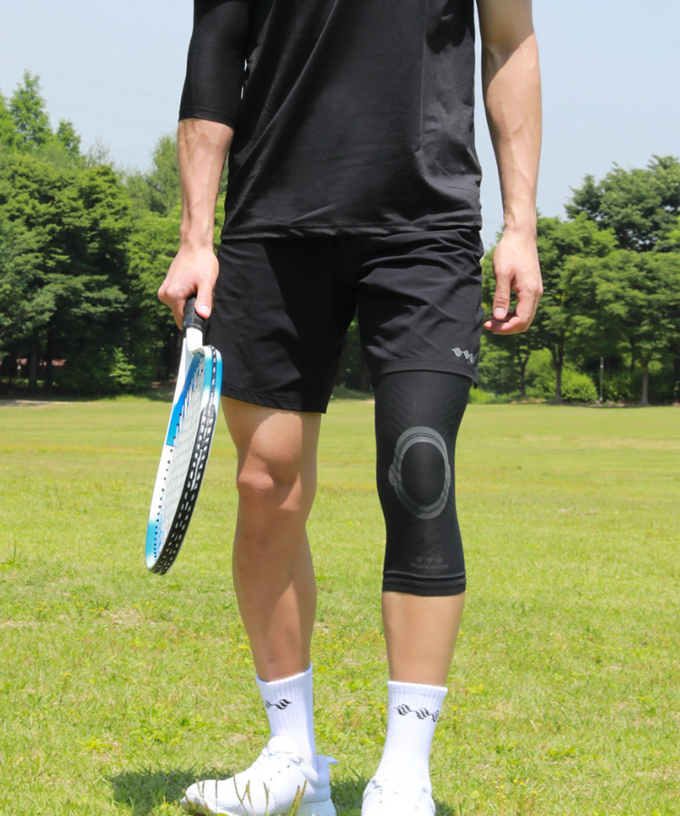 Schwarze K2 Kniebandage bei einem Tennisspieler auf dem Rasenplatz mit Schläger