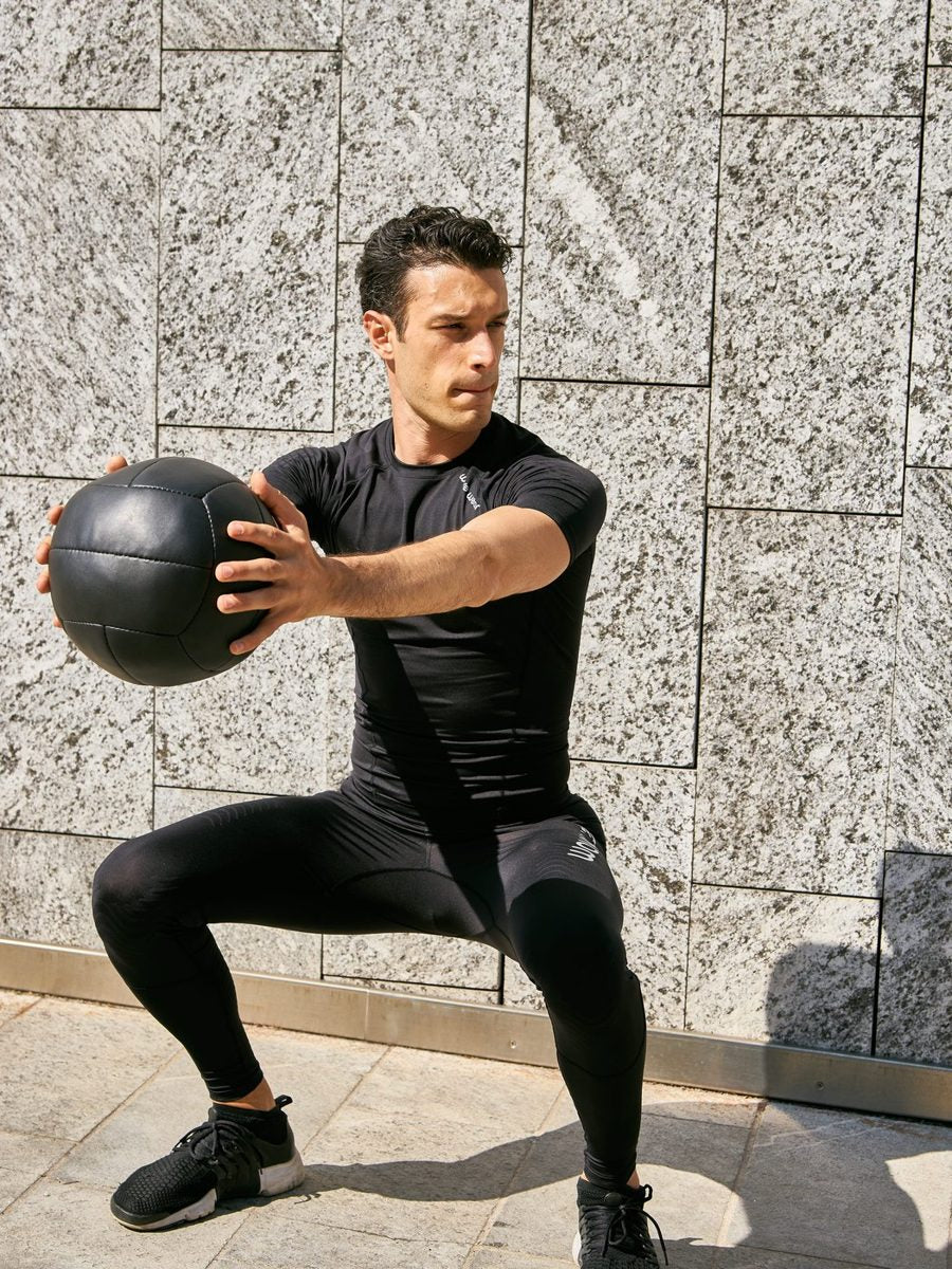 Man in a deep squat holding a medicine ball, wearing WaveWear tights