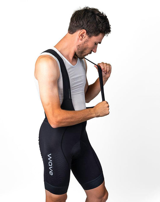 Man wearing black WaveWear compression cycling shorts for men with shoulder straps adjusting on white background